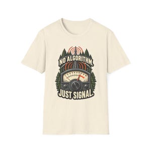 May include: A cream-colored short-sleeve t-shirt featuring a graphic of a radio signal meter and a transmission tower surrounded by pine trees. The text NO ALGORITHM is printed above the meter, and JUST SIGNAL is printed below in black.