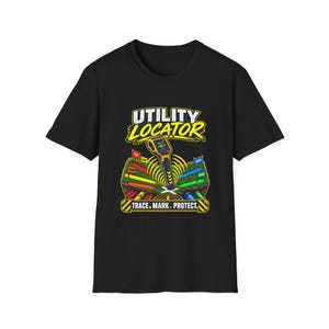 以下が含まれることがあります： 黒の半袖Tシャツ。地下のパイプと色付きの旗の上に黄色いユーティリティロケーターツールが描かれたグラフィックが特徴です。テキストには「UTILITY LOCATOR」および「TRACE. MARK. PROTECT.」と書かれています。デザインには緑の芝生と土の断面が含まれています。