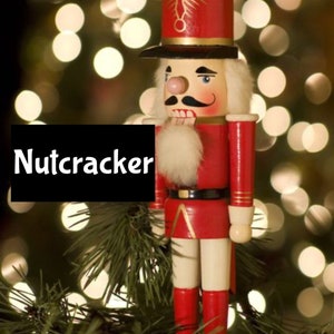 Könnte beinhalten: Eine traditionelle Holz-Nussknacker-Figur mit einer rot-weißen Uniform, einem schwarzen Hut und einem weißen Bart. Der Nussknacker steht auf einem Weihnachtsbaumzweig mit einem verschwommenen Hintergrund aus Weihnachtslichtern.