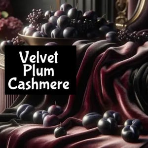 Pu&ograve; includere: Un primo piano di un tessuto di velluto rosso scuro con il testo "Velvet Plum Cashmere" in bianco. Il tessuto &egrave; drappeggiato su una ciotola di prugne e alcune prugne sono sparse sul tessuto.