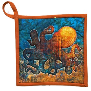 May include: Square quilted potholder featuring an octopus design in shades of orange, blue, and brown. The potholder has a loop for hanging and is trimmed with a solid orange border. A yellow pin is visible on the top edge.