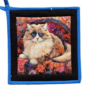 以下が含まれることがあります： 鮮やかな青い目のふわふわした猫の鮮明な画像が特徴の、正方形のキルト鍋つかみ。 猫は、鮮やかな色の花柄の表面にいます。 鍋つかみは、黒い縁取り、青いバインディング、吊り下げループが付いています。
