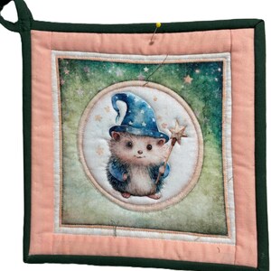 Può includere: Presina quadrata trapuntata con un design stravagante di un riccio mago. Il riccio indossa un cappello da mago blu e tiene in mano una bacchetta a forma di stella. La presina ha un bordo rosa e verde e un anello per appenderla.