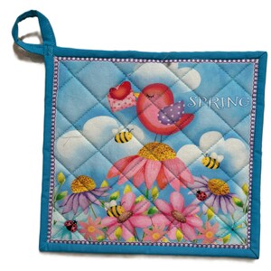 Peut inclure: Un dessous de plat carré et matelassé avec une bordure et une boucle de suspension bleues. Le motif représente un oiseau rose avec un cœur, des abeilles et des fleurs sur fond de ciel bleu. Le mot "SPRING" est imprimé en haut à droite.