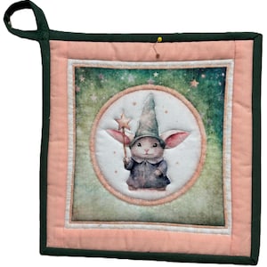 Può includere: Un presina quadrata e trapuntata con un design stravagante. Il centro presenta un'illustrazione ad acquerello di un coniglio vestito da mago, con in mano una bacchetta a stella. La presina ha un bordo rosa, finiture verdi e un anello verde per appenderla.