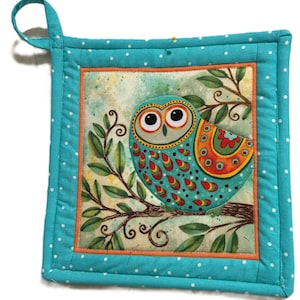 Könnte beinhalten: Quadratischer, gesteppter Topflappen mit einem farbenfrohen Eulenmuster. Die Eule mit großen Augen ist mit roten, orangefarbenen und türkisfarbenen Mustern verziert und sitzt auf einem Ast. Der Topflappen hat einen türkisfarbenen Rand mit weißen Punkten und eine Aufhängeschlaufe.