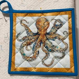 May include: A blue and yellow quilted hot pad with an octopus design. The octopus is brown and white with intricate details.