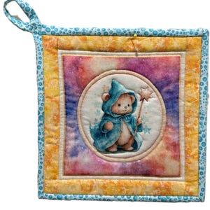 Può includere: Un presina quadrata trapuntata con un design stravagante. Il centro presenta un orsacchiotto in costume da mago blu con una bacchetta a stella, su uno sfondo di galassia colorata. Ha un anello blu per appenderla.