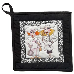 Può includere: Presina trapuntata nera con anello per appenderla. Il centro presenta un'illustrazione stravagante di due chef donne in uniformi bianche e cappelli da chef, che tengono utensili da cucina. Il bordo è bianco con pois neri.