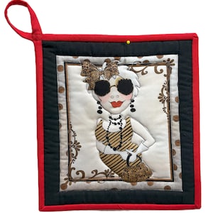 May include: A quilted hot pad featuring a stylish woman with sunglasses, a bow, and a leopard print outfit. The pad has a red border, black accents, and a loop for hanging. The design is centered on a cream background with brown accents.