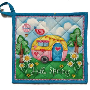 May include: A quilted pot holder with a teal border and hanging loop. The design features a yellow and pink caravan with a blue door, hearts, and a bird on top. The background includes trees, daisies, a hot air balloon, and the words "Hello Spring".