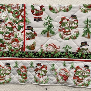 May include: A white quilted fabric with a Christmas theme. The fabric features a repeating pattern of snowmen, Christmas trees, holly, and the word "Miracle".