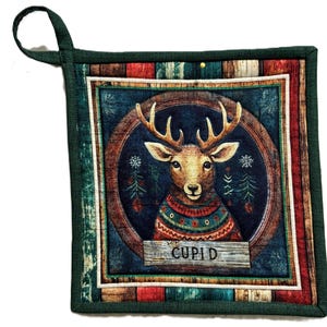May include: Square quilted pot holder with a deer wearing a sweater, the word "Cupid" on a wooden sign, and a green hanging loop. The deer is set against a blue background with a wooden frame and a border of red, white, and green.