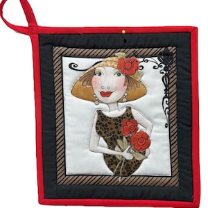 May include: Quilted pot holder featuring a whimsical illustration of a woman in a hat holding red flowers. The design includes a black and brown border, a red trim, and a loop for hanging. The woman is wearing a leopard print dress.