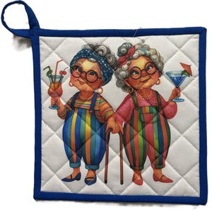 Puede incluir: Manopla acolchada con borde y lazo para colgar azules. El diseño presenta a dos mujeres mayores sosteniendo cócteles, usando gafas y monos a rayas de colores. El fondo es blanco con un patrón de diamantes.