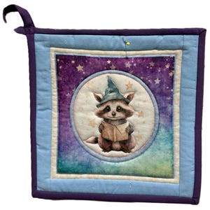 Può includere: Un presina quadrata trapuntata con un design stravagante. Il centro presenta un procione con un cappello da mago e un libro, su uno sfondo viola stellato. La presina ha un bordo azzurro e viola, con un anello per appenderla.