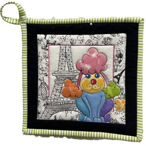 May include: A square fabric potholder featuring a black and white line drawing of the Eiffel Tower and floral patterns. A colorful, appliqued poodle with a pink head, yellow face, and blue body sits in the foreground with orange and green accents.