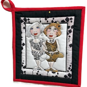 May include: A quilted potholder featuring a whimsical illustration of two women in dresses. The potholder has a red border, black accents, and a white background with black spots. The women are holding hands and wearing jewelry.