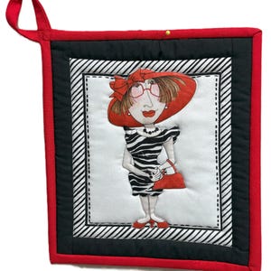 May include: A quilted hot pad featuring a whimsical illustration of a woman in a red hat and zebra-striped dress, holding a red purse. The pad has a red border, black accents, and a hanging loop.