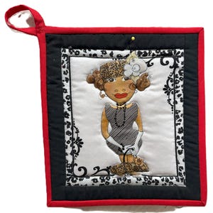 May include: A quilted hot pad with a red border and a black and white patterned frame. The center features a cartoon illustration of a woman in a gray dress, gloves, and a leopard print hat and shoes. A red loop is attached for hanging.