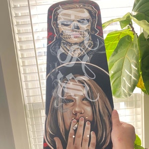 Może przedstawiać: Deska skateboardowa z namalowanym wzorem przedstawiającym osobę z czaszką na twarzy i kobietę palącą papierosa. Tło jest czerwone i czarne z białymi akcentami.