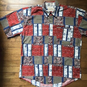 May include: Short-sleeved button-down shirt with a patchwork design. The shirt features red, navy blue, and khaki squares with golf ball and paisley patterns. The collar has the text "Nautica Golf".