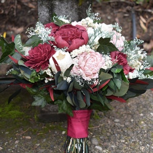 May include: A bouquet of burgundy, blush pink, and white silk flowers with greenery and a burgundy ribbon.