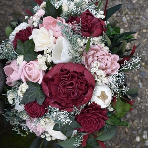 May include: A bouquet of burgundy and blush-colored silk flowers with greenery and white baby's breath.