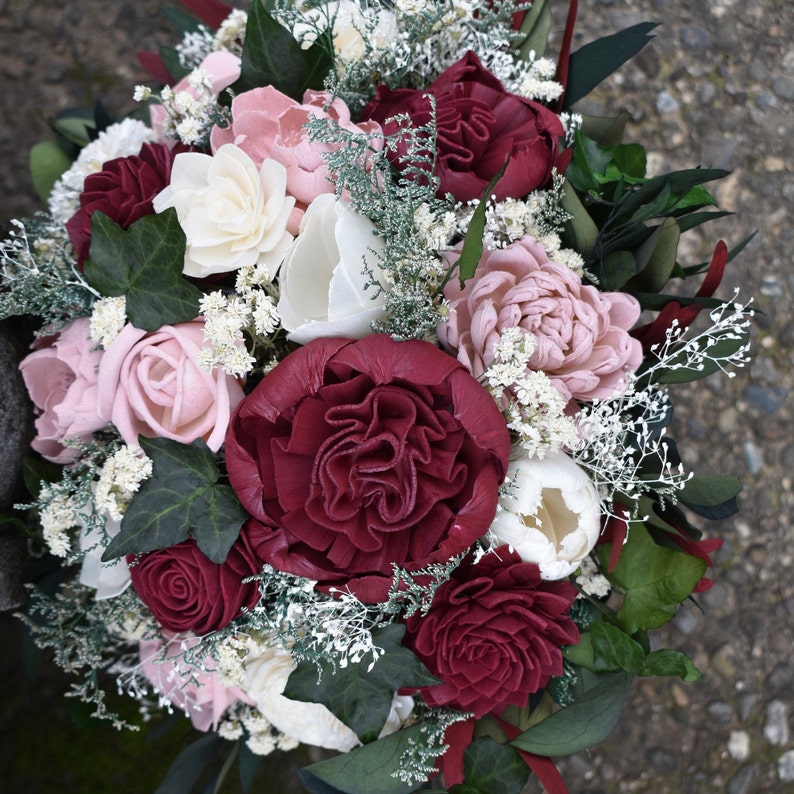 May include: A bouquet of burgundy and blush-colored silk flowers with greenery and white baby's breath.