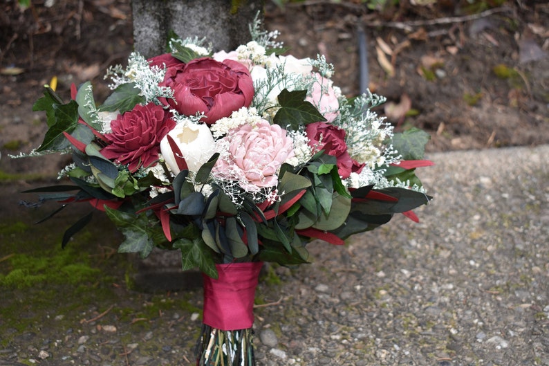 May include: A bouquet of burgundy, blush pink, and white silk flowers with greenery and a burgundy ribbon.