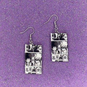 May include: A pair of silver dangle earrings with black and white manga panels featuring characters from the anime My Hero Academia. The panels show the characters Izuku Midoriya, Katsuki Bakugo, and All Might.