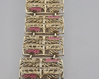 May include: Gold-tone bracelet with rectangular links featuring a floral design and pink enamel accents. The bracelet is composed of multiple connected segments, creating a flexible and decorative accessory.
