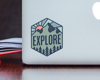 May include: A hexagonal sticker with a mountain range, a sun, and trees in shades of green, blue, and orange. The sticker says "EXPLORE" in a white outline.