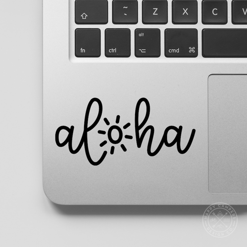 May include: A black and white sticker with the word "Aloha" written in a cursive font with a sun graphic in the middle of the word. The sticker is on a silver laptop.