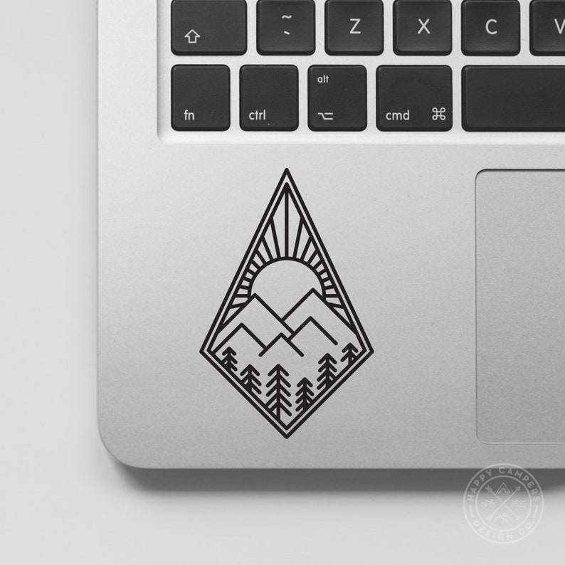 May include: Black and white line art sticker of a mountain range with a sun and trees. The sticker is on a silver laptop.