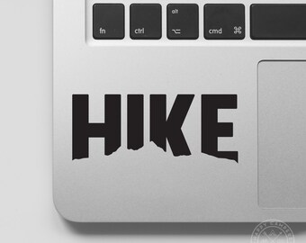 May include: Black vinyl sticker with the word "HIKE" in bold, block letters. The letters are cut out to reveal a mountain range silhouette.