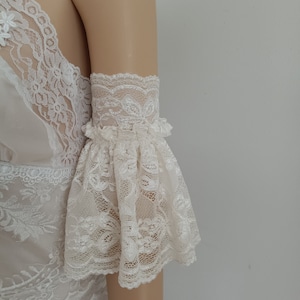 May include: White lace lingerie top with a ruffled, bell-shaped sleeve. The top is made of delicate, sheer lace with a floral pattern.