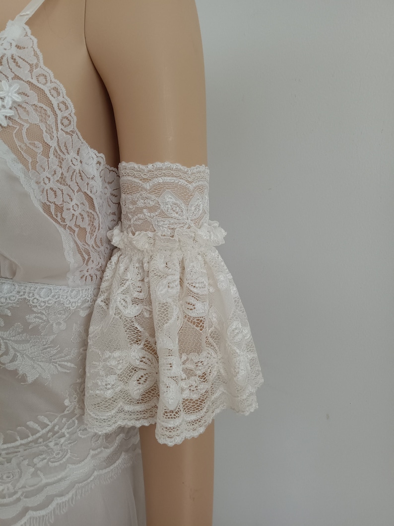 May include: White lace lingerie top with a ruffled, bell-shaped sleeve. The top is made of delicate, sheer lace with a floral pattern.