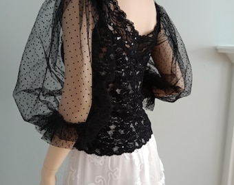 May include: Black lace top with sheer polka dot sleeves. The top has a square neckline and is fitted. The sleeves are long and puffy. The top is paired with a white skirt with a layered design.