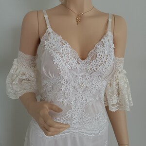 May include: White lace dress with a delicate floral pattern and a V-neckline. The dress has short, ruffled sleeves and a flowing skirt.