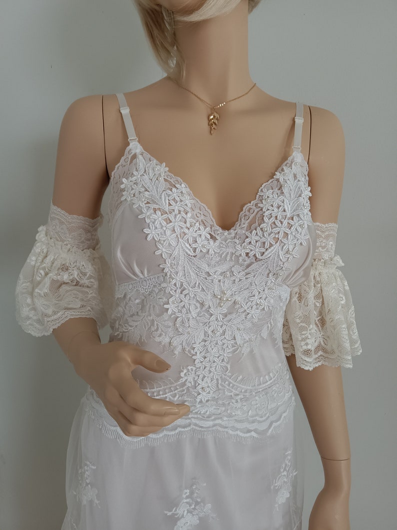 May include: White lace dress with a delicate floral pattern and a V-neckline. The dress has short, ruffled sleeves and a flowing skirt.