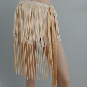 May include: A cream-coloured fringe skirt with a lace waistband and a satin ribbon tie. The skirt is made of long, vertical strands of fabric, creating a flowing, textured look. The skirt is a bohemian style.