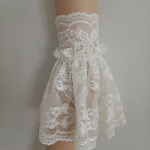 May include: White lace cuff with a ruffled edge. The lace has a floral pattern.