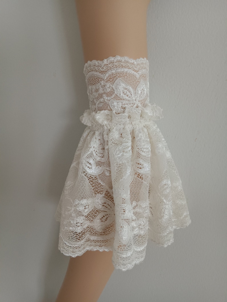May include: White lace cuff with a ruffled edge. The lace has a floral pattern.