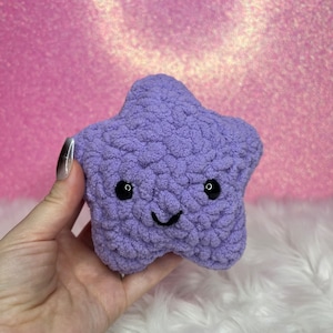 May include: A purple plush star-shaped toy with a smiling face. The toy has black eyes and a black stitched smile.