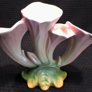 May include: A pink and green ceramic flower vase with three trumpet-shaped openings. The vase is in the shape of three stylized flowers.