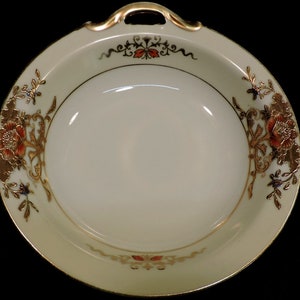 May include: A white porcelain bowl with gold and red floral designs. The bowl has two handles and a scalloped rim.
