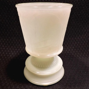 May include: A white opaque glass vase with a fluted base and a wide, flared top. The vase has a textured, swirling design.