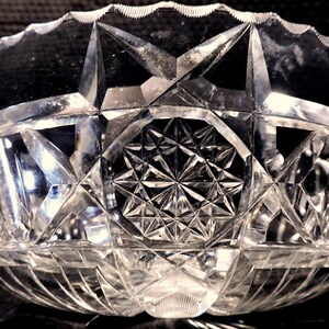 May include: A clear glass bowl with a cut glass design. The bowl has a starburst pattern in the center and a geometric pattern around the rim.