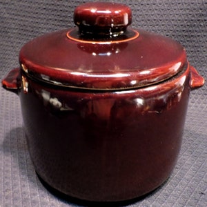 May include: A brown ceramic bean pot with a lid. The pot has two handles on the sides and a knob on the lid.
